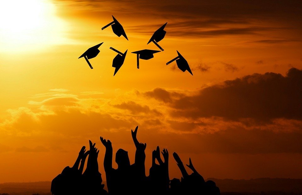 In the shadows of the sun, graduates throw their caps into the air