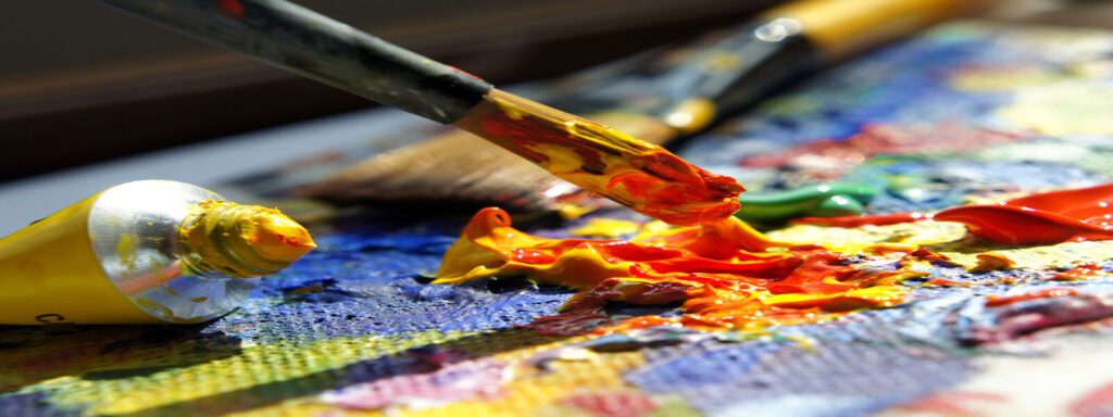 A paintbrush dips into vibrant oil paints